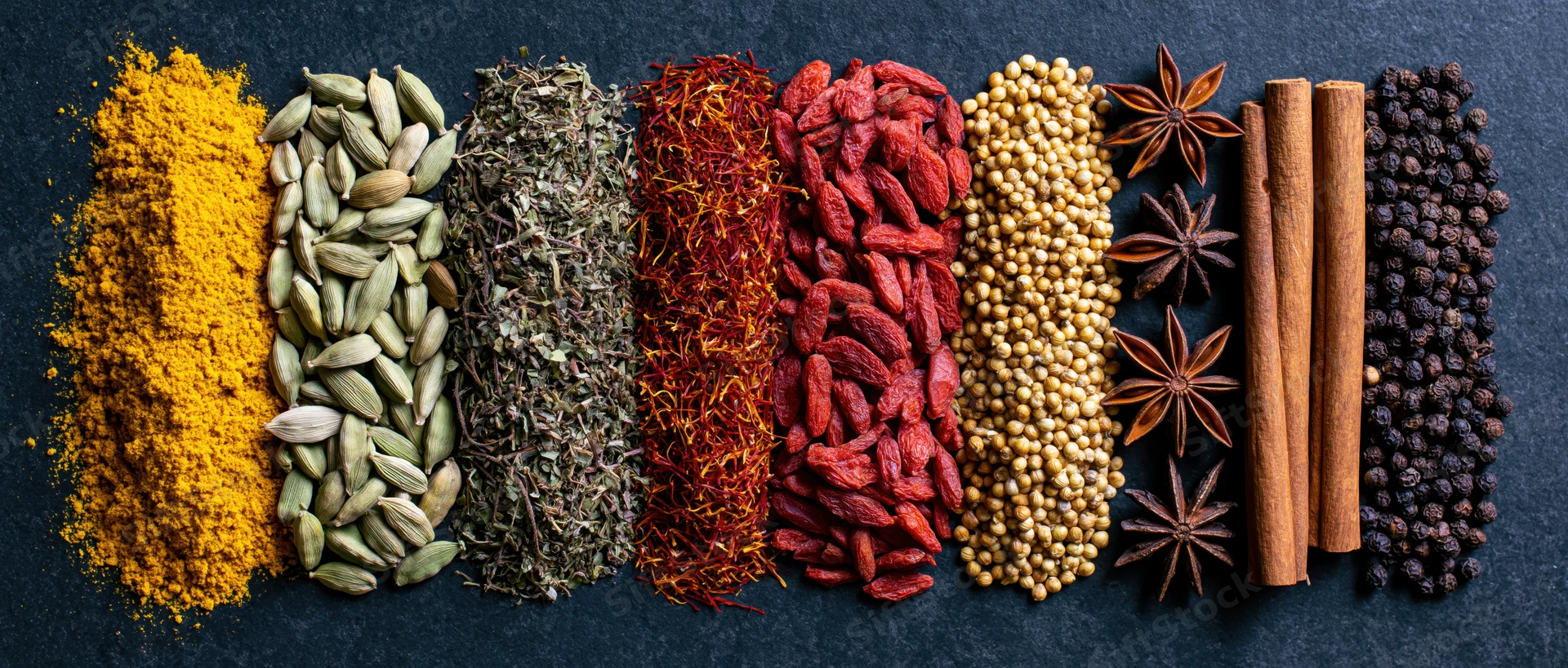 Assorted spices arranged in parallel vertical rows on dark textured surface