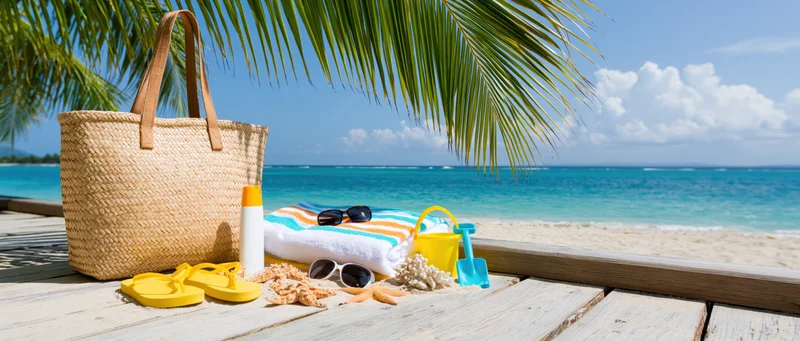 Beach accessories arranged on wooden deck beside sandy shore with ocean and palm fronds in background