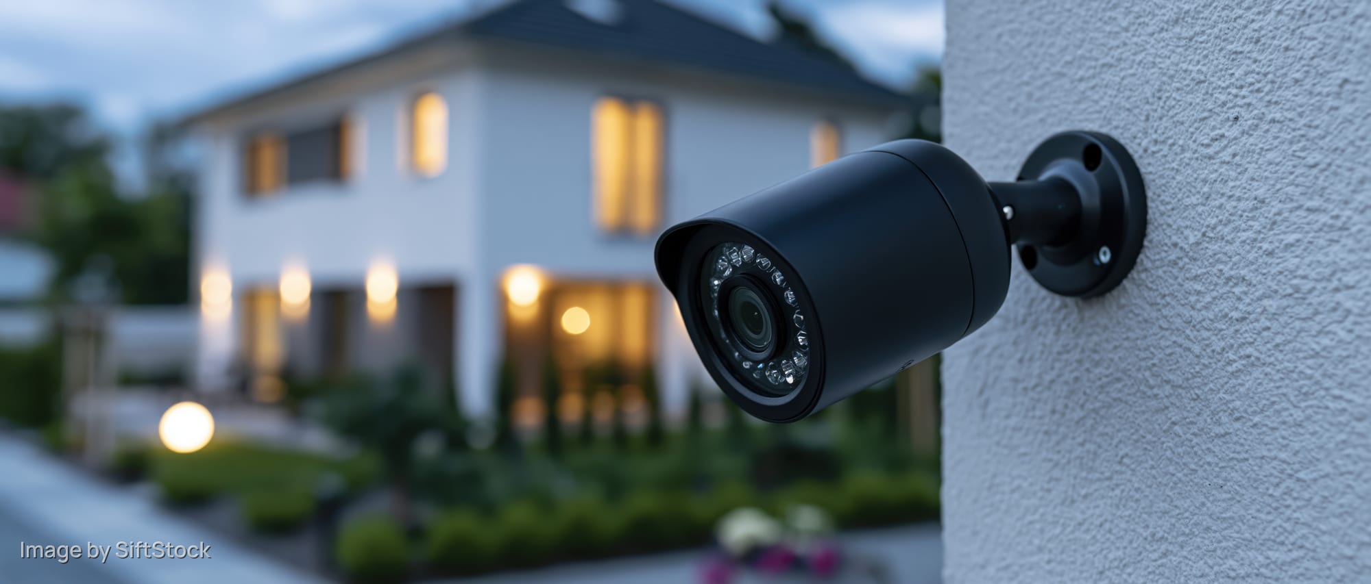 Black bullet-style security camera mounted on a house exterior wall at dusk