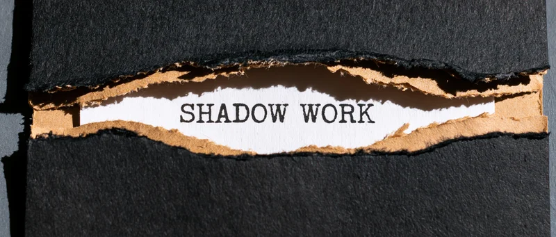 Torn black cardboard revealing the words shadow work on white paper beneath