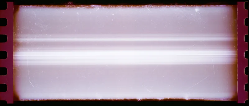 Overexposed 35mm film frame with light leak and damage showing blank white area and perforated edges