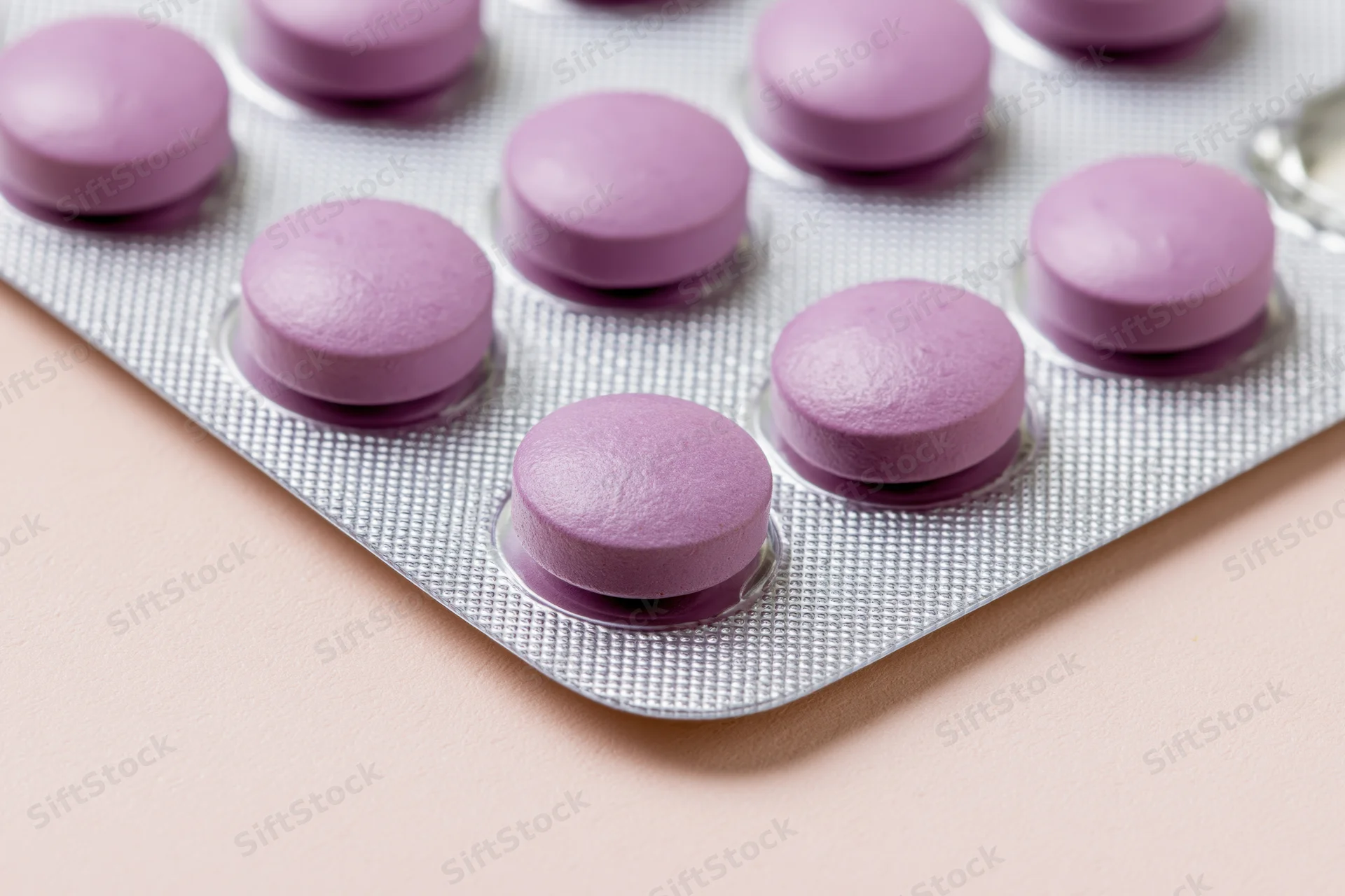 Round purple pills in a blister pack on a pale pink surface