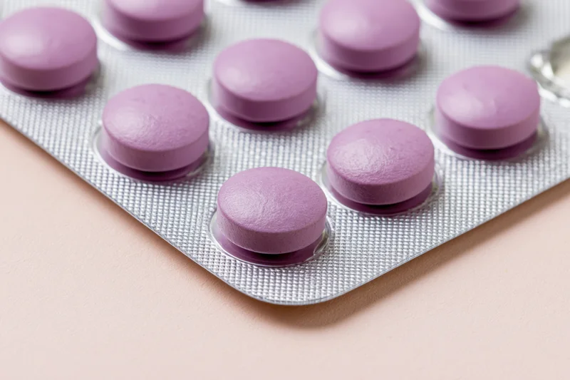Round purple pills in a blister pack on a pale pink surface