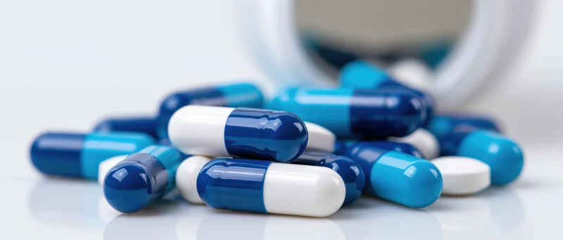 Blue and white medication capsules scattered on a white surface near a bottle