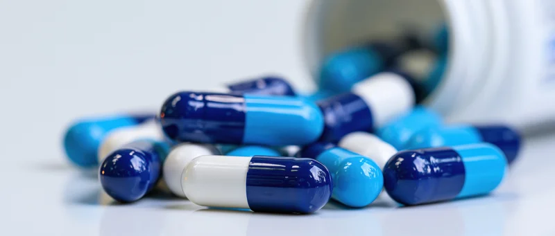 Blue and white medication capsules scattered on a white surface near a bottle