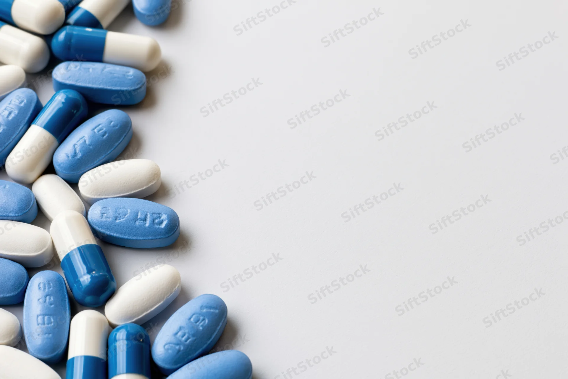 Blue and white oval pills scattered along the left edge on a plain surface