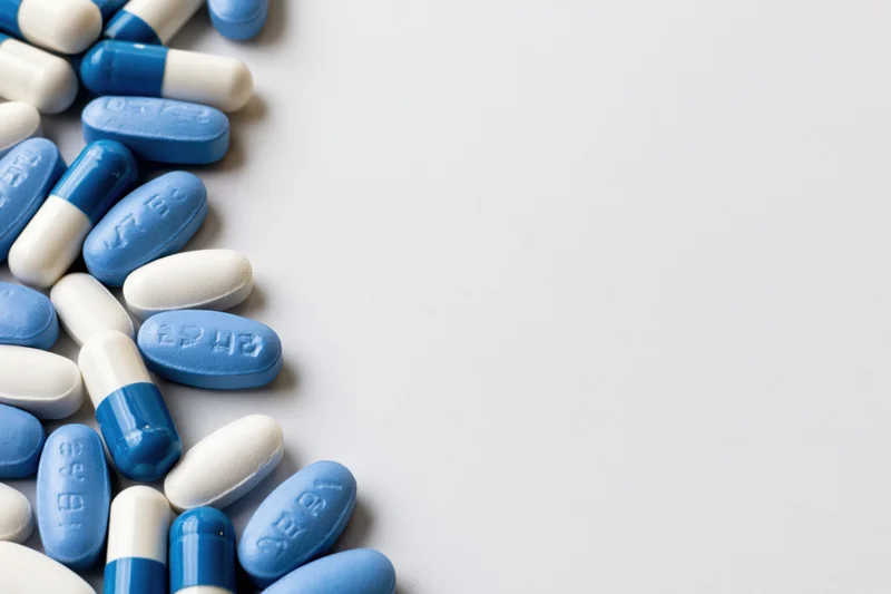 Blue and white oval pills scattered along the left edge on a plain surface