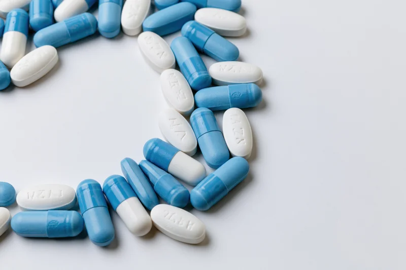 Blue and white oval pills scattered along the left edge on a white surface