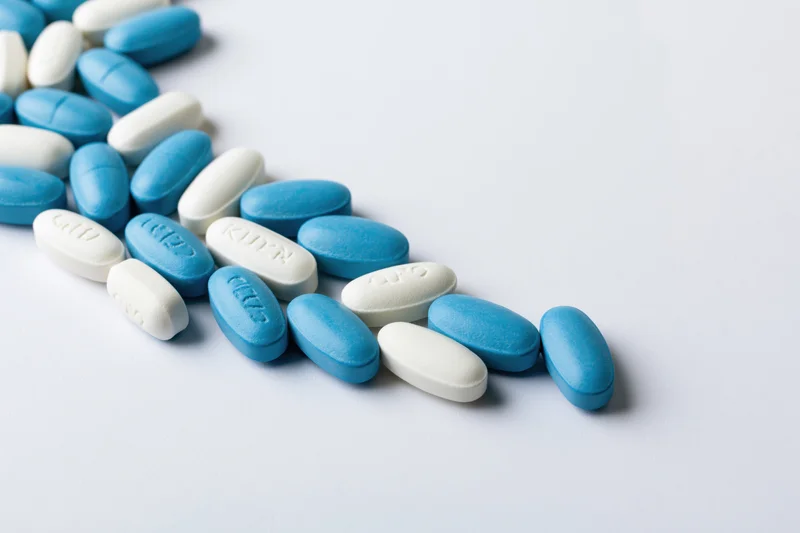 Blue and white oval pills scattered along the left edge on a white surface