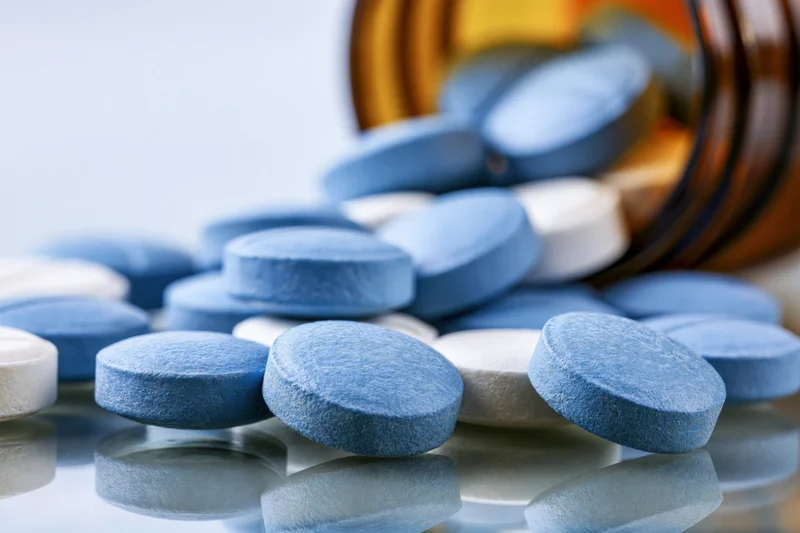 Blue and white round tablets spilled from an amber glass bottle onto a reflective surface