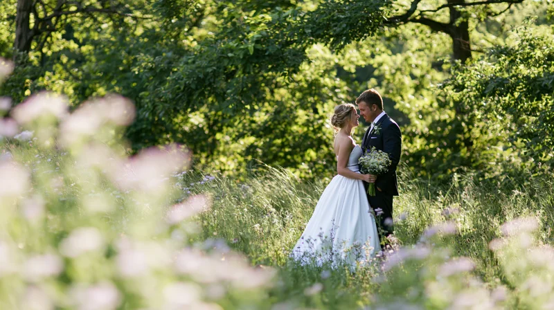 Bride and groom standing close together in a sunlit garden surrounded by greenery and wildflowers