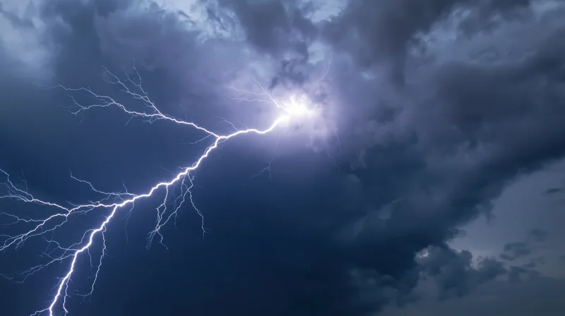 Bright lightning bolt splitting across a dark stormy sky at night