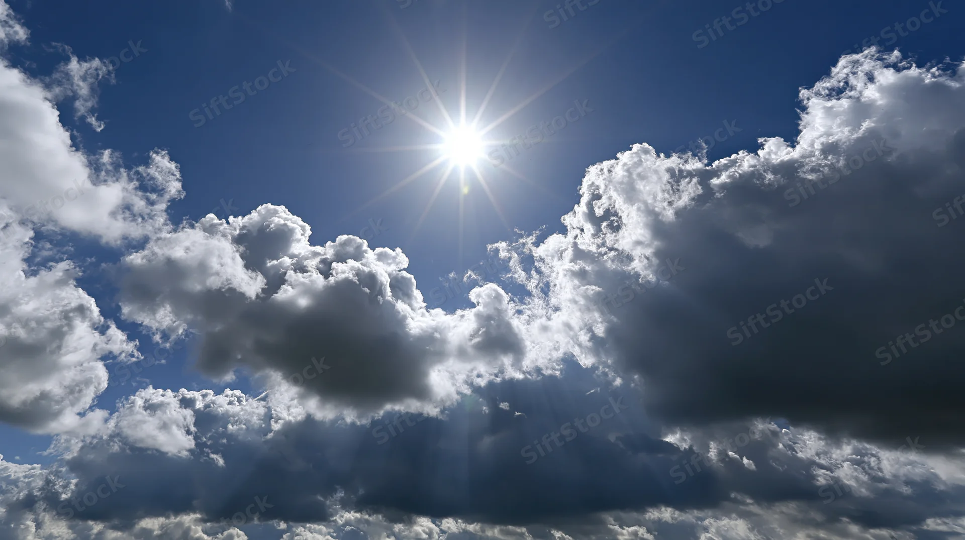 Bright sun shining through dramatic cumulus clouds in a blue sky