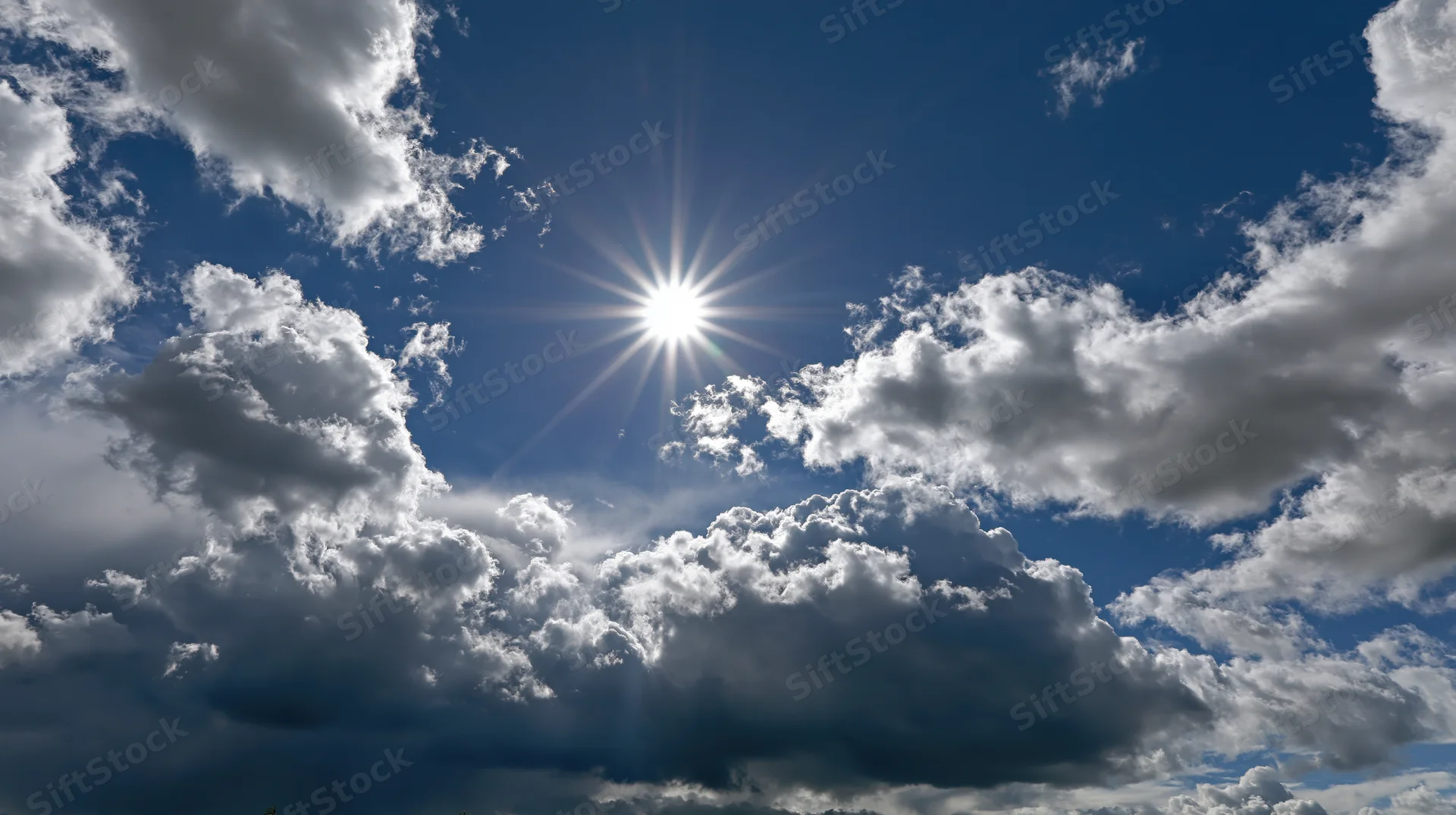 Bright sun shining through dramatic cumulus clouds in a blue sky