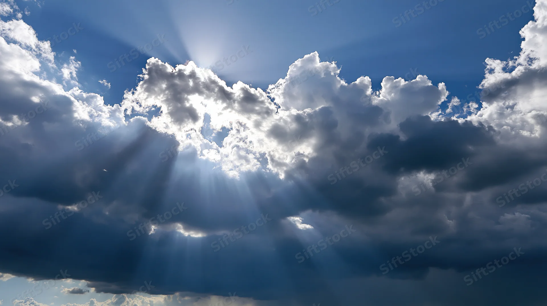Sunbeams breaking through dramatic cumulus clouds in a bright blue sky