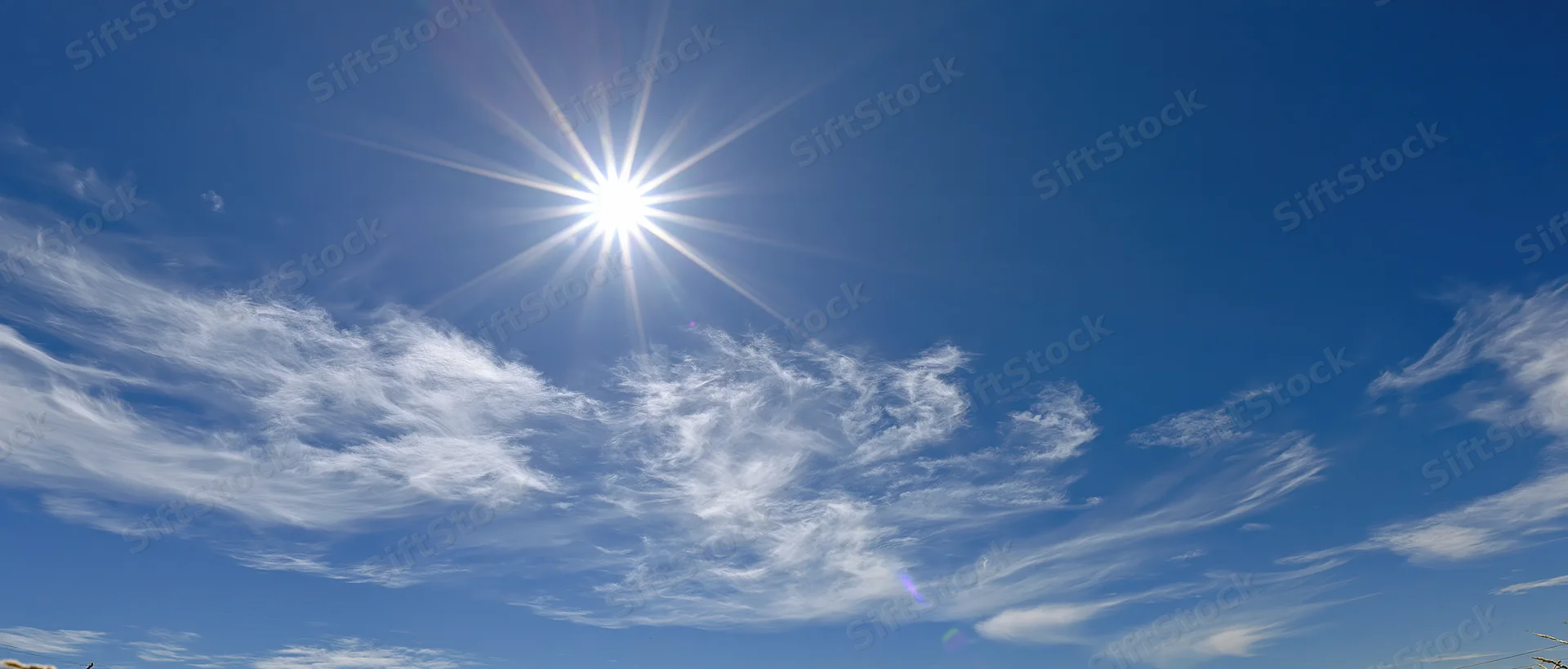 Bright sun with starburst lens flare in a blue sky with wispy clouds at midday
