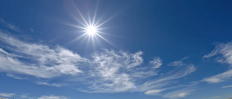 Bright sun with starburst lens flare in a blue sky with wispy clouds at midday