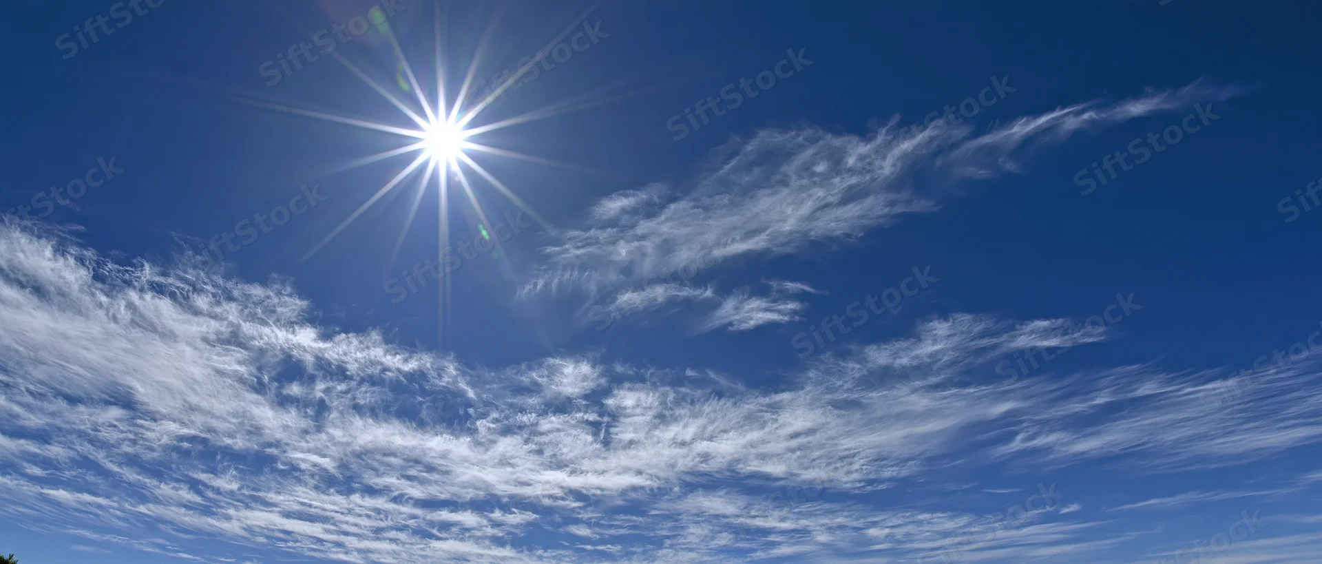 Bright sun with starburst lens flare in a blue sky with wispy white clouds during midday