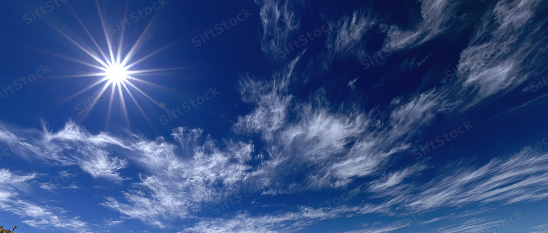 Bright midday sun with starburst lens flare and wispy white clouds in a deep blue sky