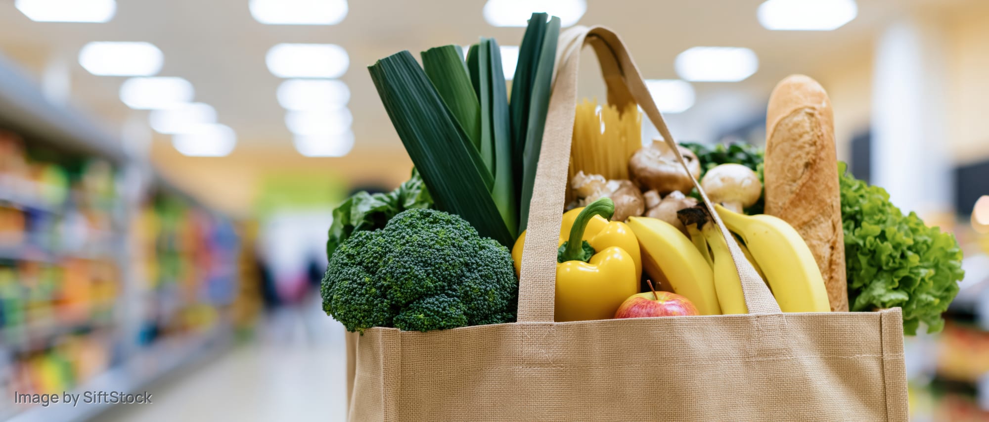Reusable shopping bag filled with fresh produce and groceries in a supermarket aisle