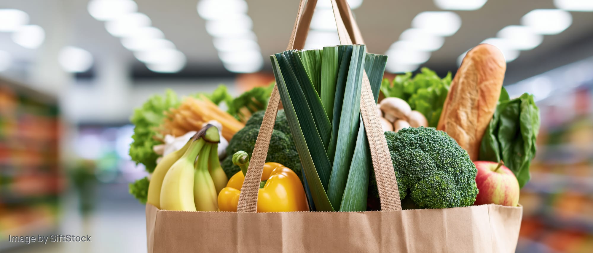 Brown reusable shopping bag filled with fresh vegetables and fruits in a supermarket aisle