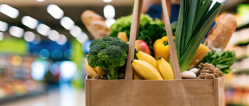 Reusable shopping bag filled with fresh produce and groceries in a supermarket