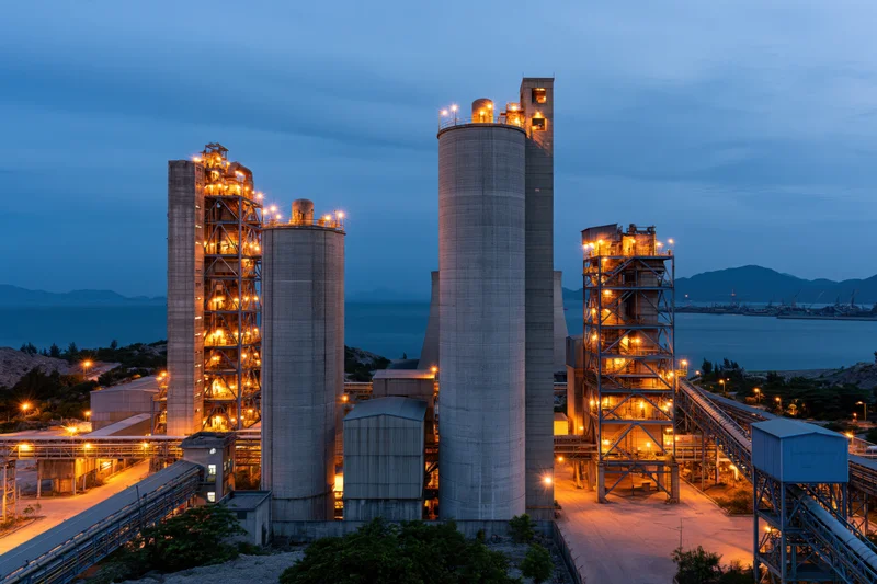 Cement plant with tall concrete silos and industrial towers at twilight by the coast