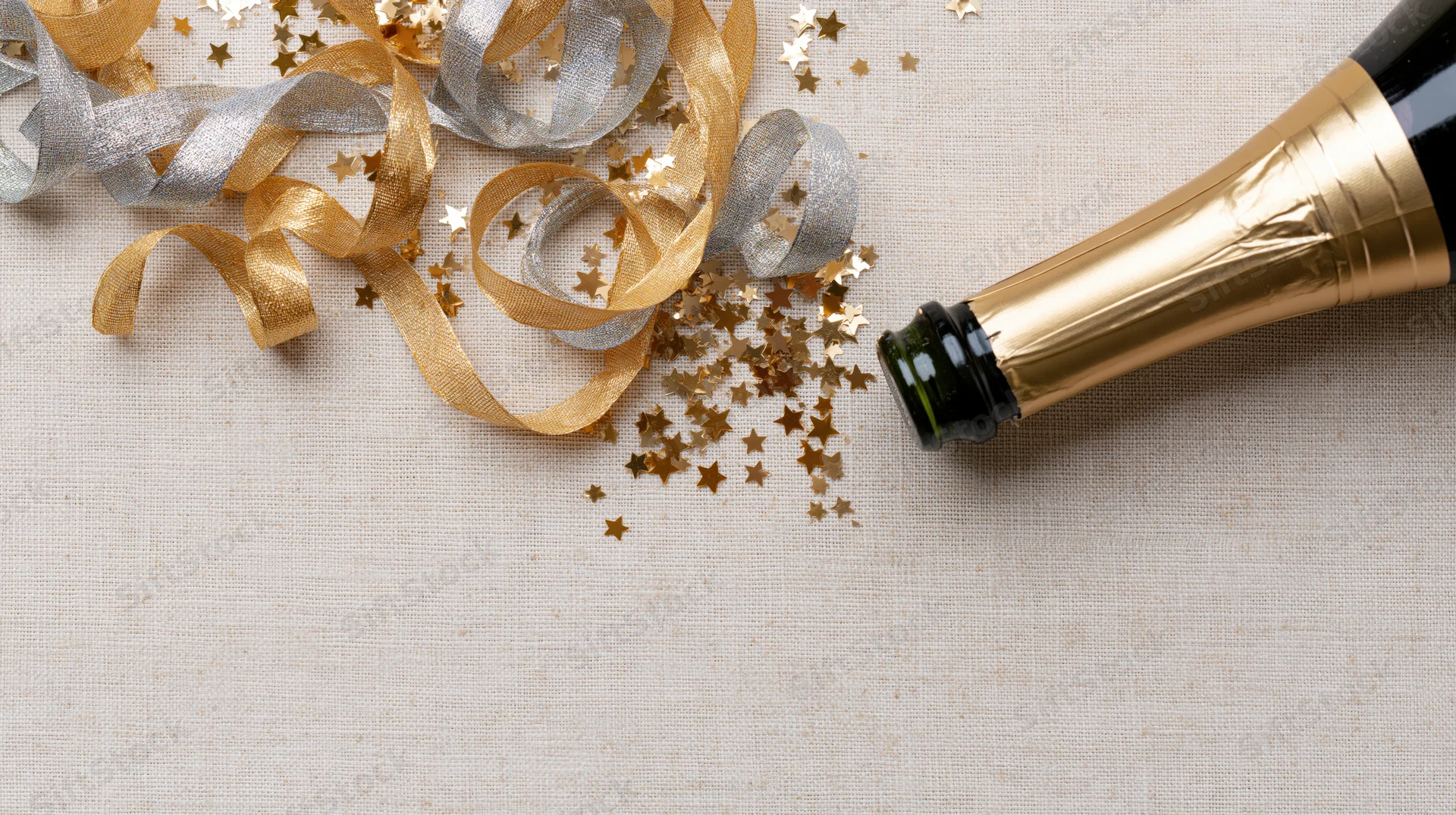 Champagne bottle lying on its side with gold and silver ribbons and star confetti on a linen surface