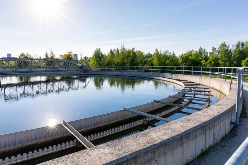 Circular clarifier tank in wastewater treatment plant with sunlight reflecting on calm water surface