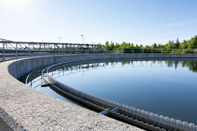 Circular clarifier tank at a wastewater treatment facility under clear sky