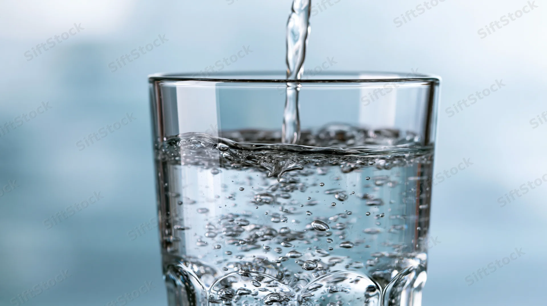 Water being poured into a clear drinking glass against a light blue background