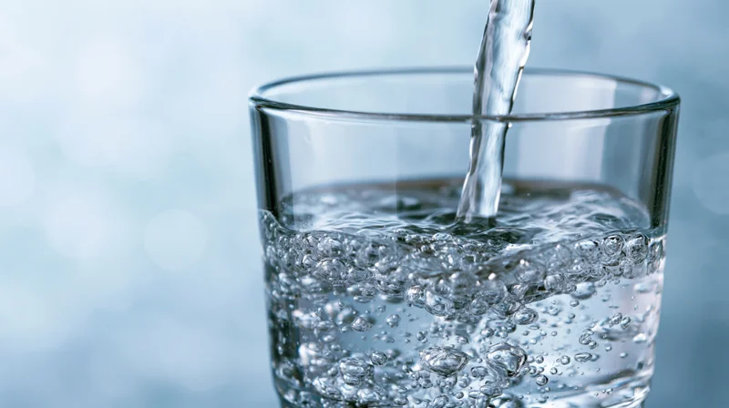 Water being poured into a clear glass on a light blue background