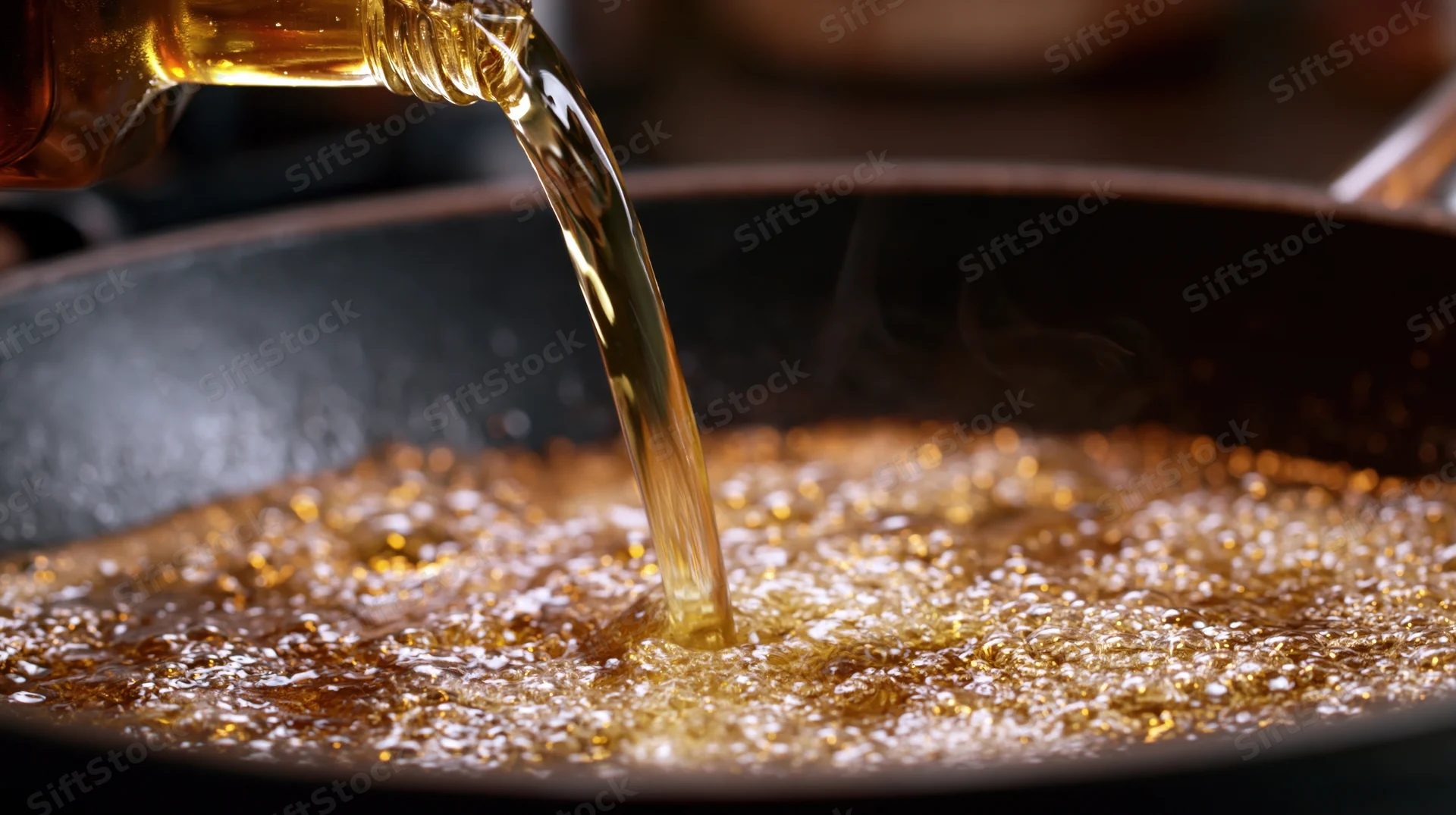 Golden oil pouring from a glass bottle into a hot nonstick frying pan