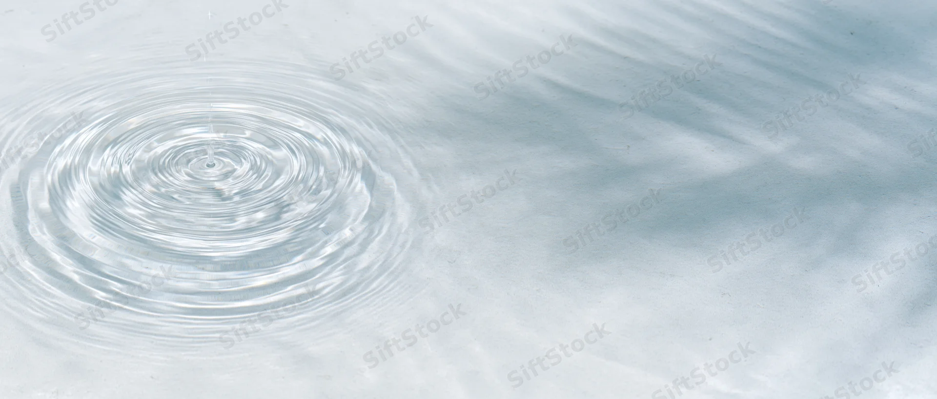 Clear shallow water surface with concentric ripples from a droplet, viewed from above