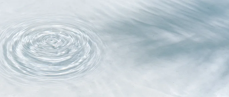 Clear shallow water surface with concentric ripples from a droplet, viewed from above