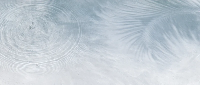 Concentric ripples spreading across shallow clear water surface from a droplet impact