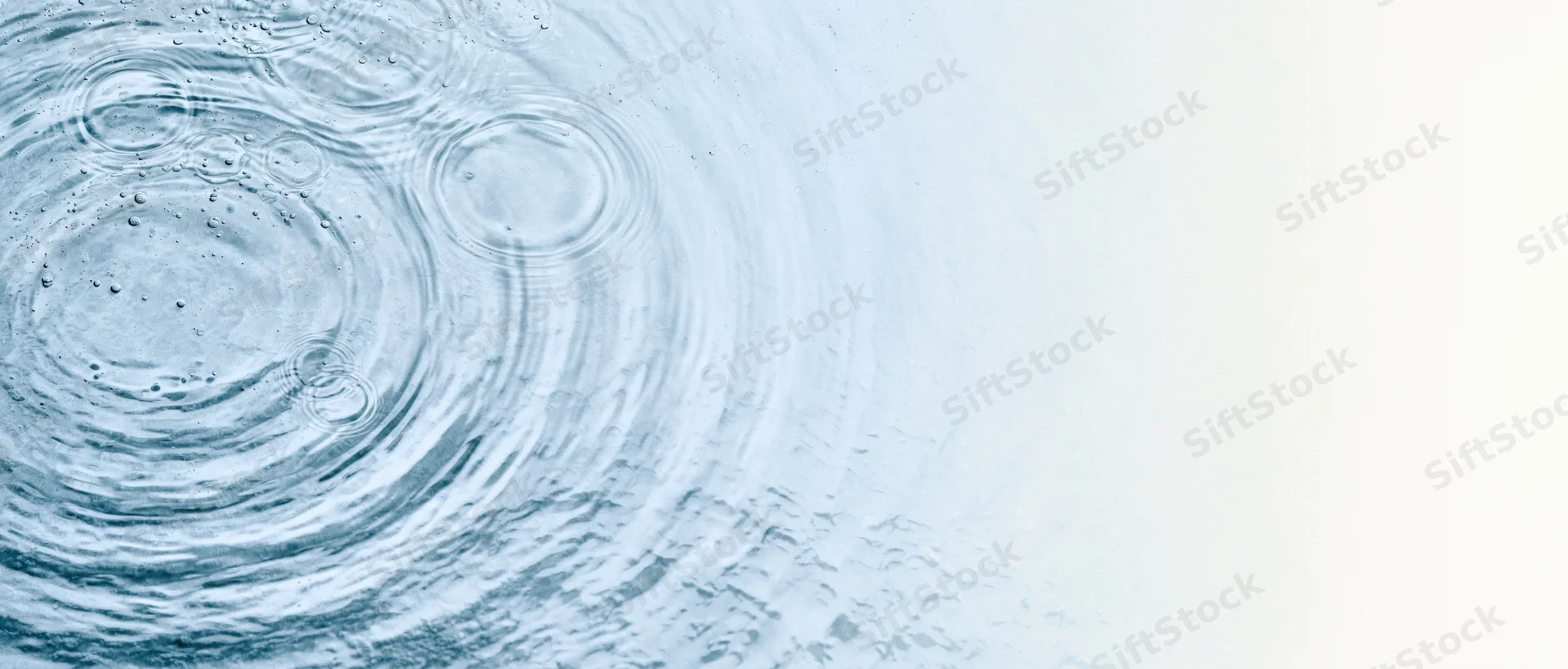 Overhead view of rippling water surface with concentric circles and droplets on left, fading to white on right