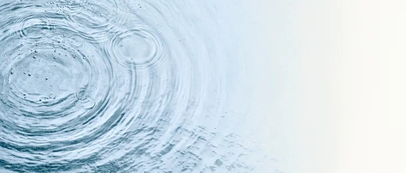 Overhead view of rippling water surface with concentric circles and droplets on left, fading to white on right