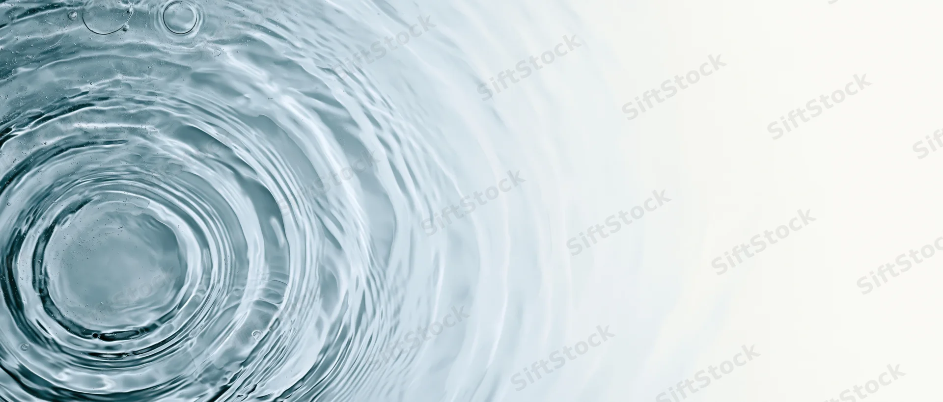 Overhead view of rippling water surface with concentric circles and bubbles on left, white background on right