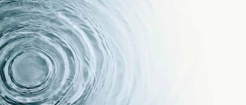 Overhead view of rippling water surface with concentric circles and bubbles on left, white background on right