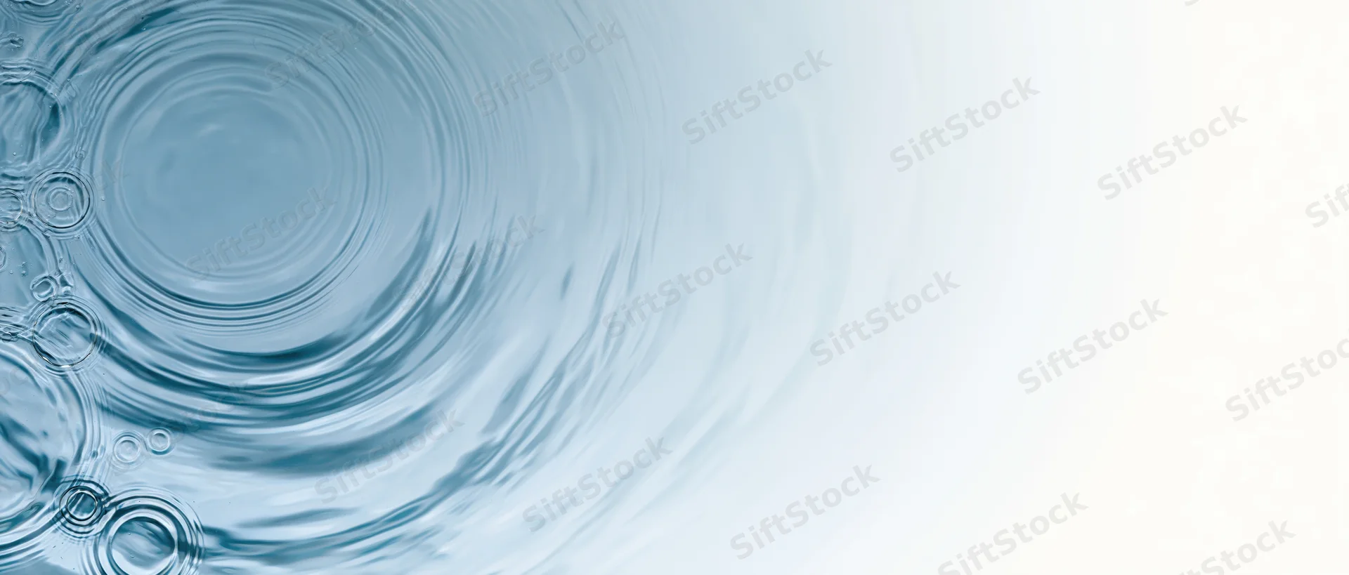 Water surface with concentric ripples and droplets on left, fading to white on right