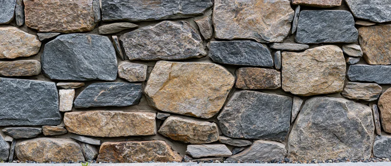Close-up of a dry-stacked rubble stone wall with irregularly shaped stones in gray and brown tones