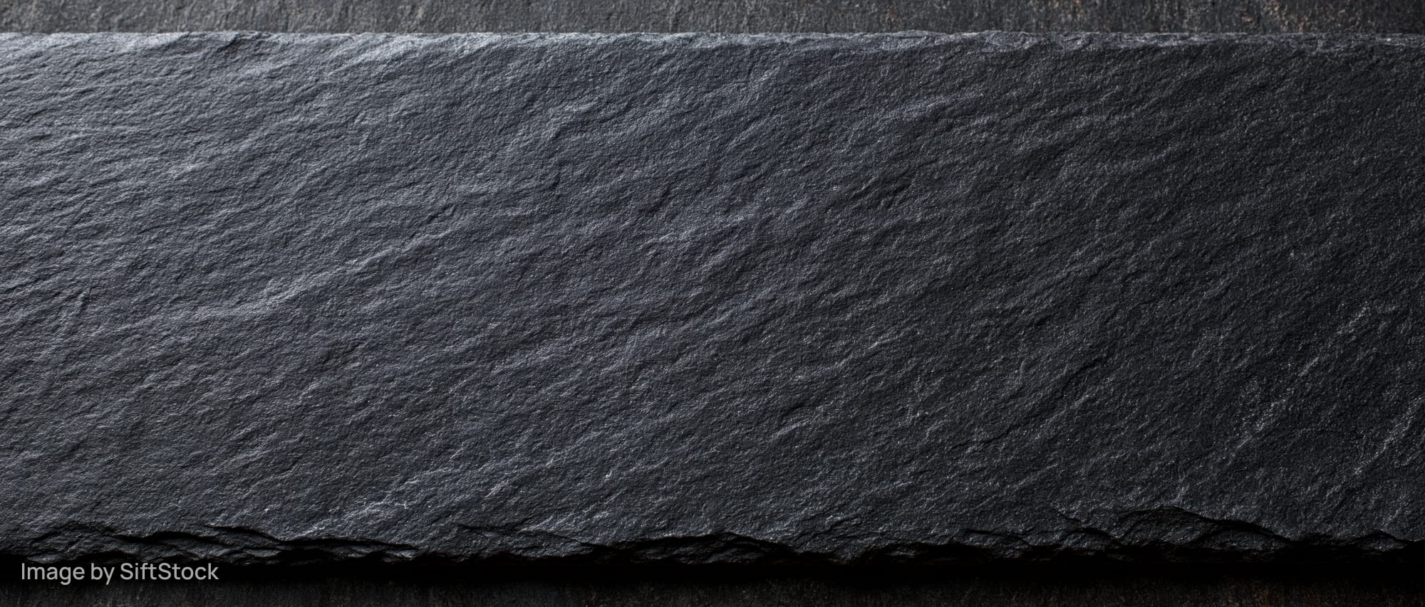 Close-up of dark natural slate stone surface with rough texture and uneven edges