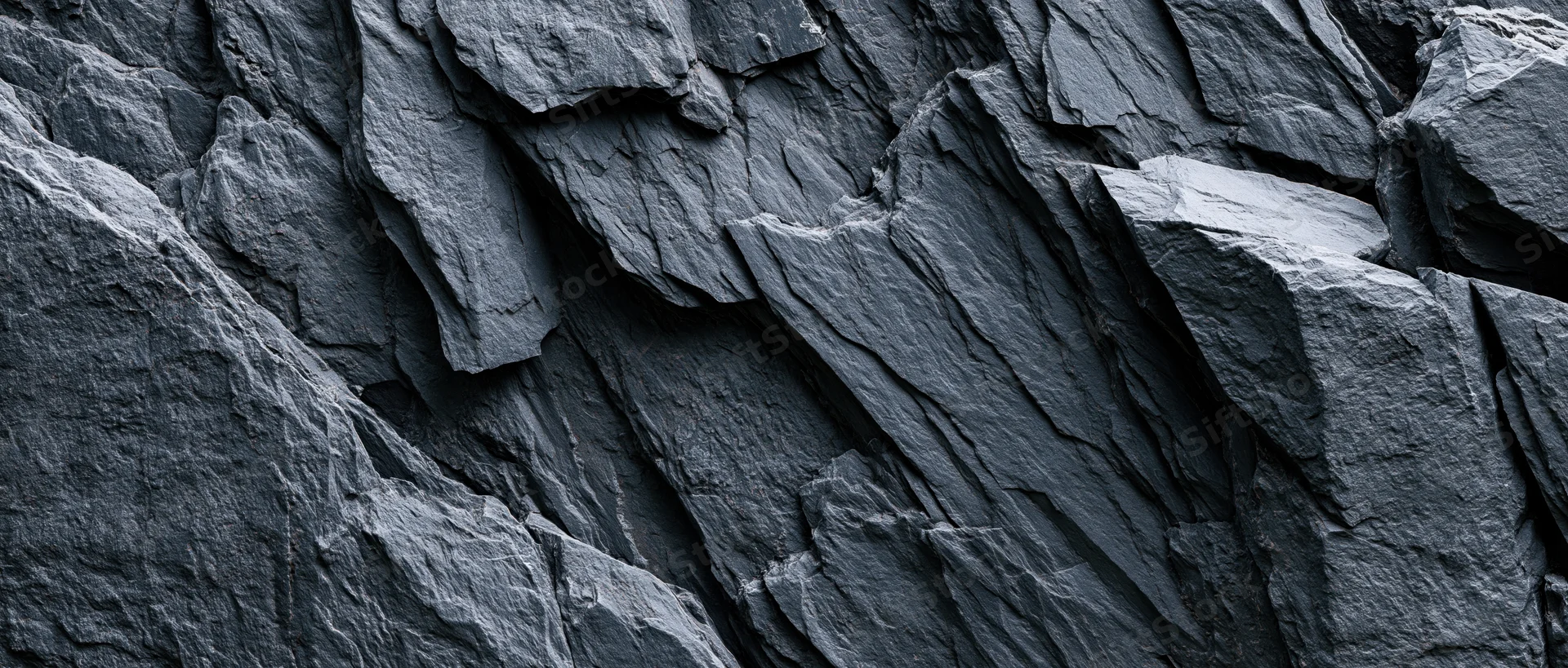 Close-up of dark slate rock face with layered fractures and rugged texture