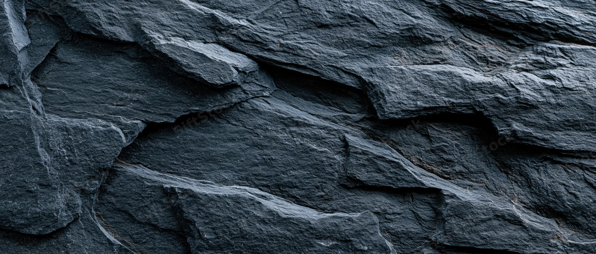 Close-up of dark slate rock face with layered fractures and rough texture filling the frame
