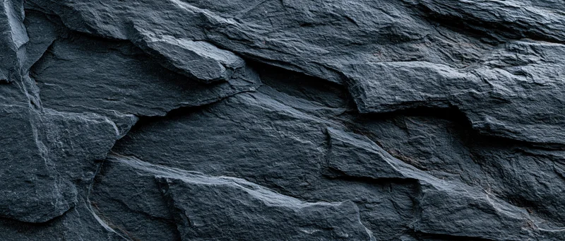 Close-up of dark slate rock face with layered fractures and rough texture filling the frame