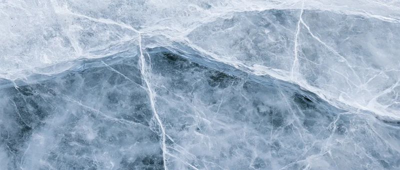 Close-up of natural ice surface with cracks and blue-gray textures filling the frame