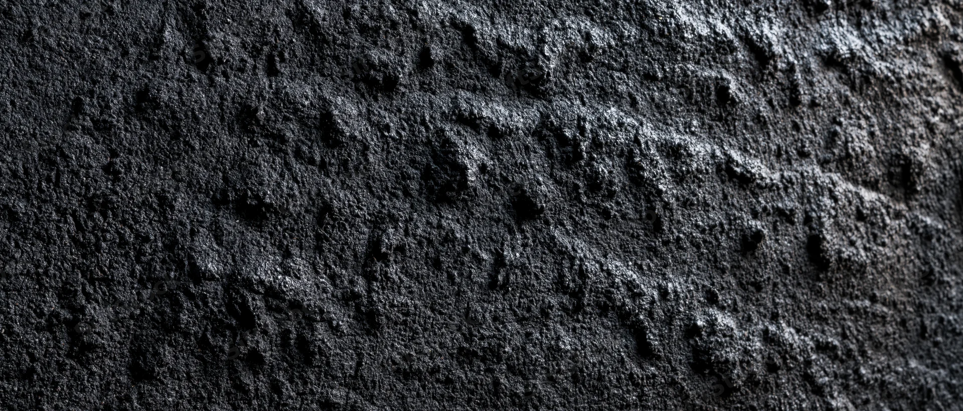 Close-up of rough dark concrete wall surface with textured grain and shadowed depth
