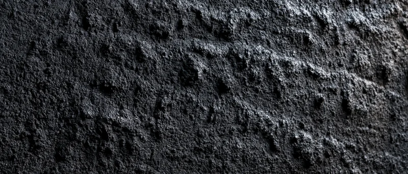 Close-up of rough dark concrete wall surface with textured grain and shadowed depth