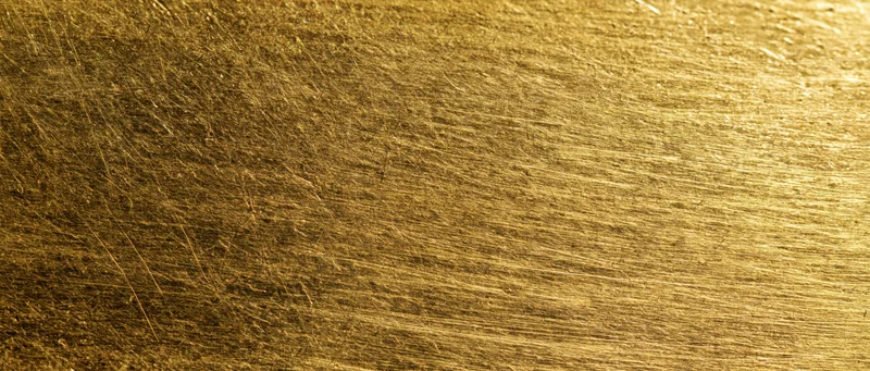 Close-up of scratched gold metal surface with linear texture and reflective highlights